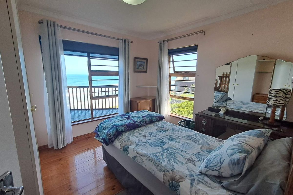 A bedroom featuring hardwood flooring, louvered windows, and direct access to a balcony with ocean views.