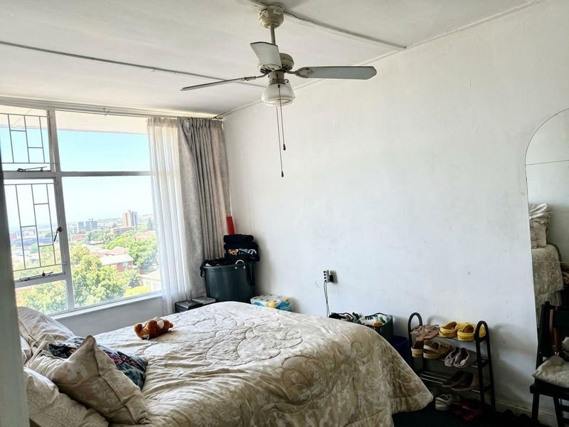 A bedroom featuring a ceiling fan and a large window with security bars, offering an elevated view of the surrounding area.