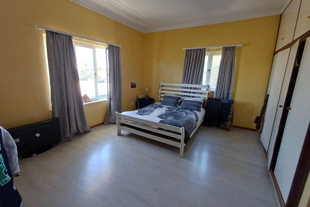 A spacious bedroom featuring light-toned laminate flooring, built-in wardrobes, and dual windows providing natural light.