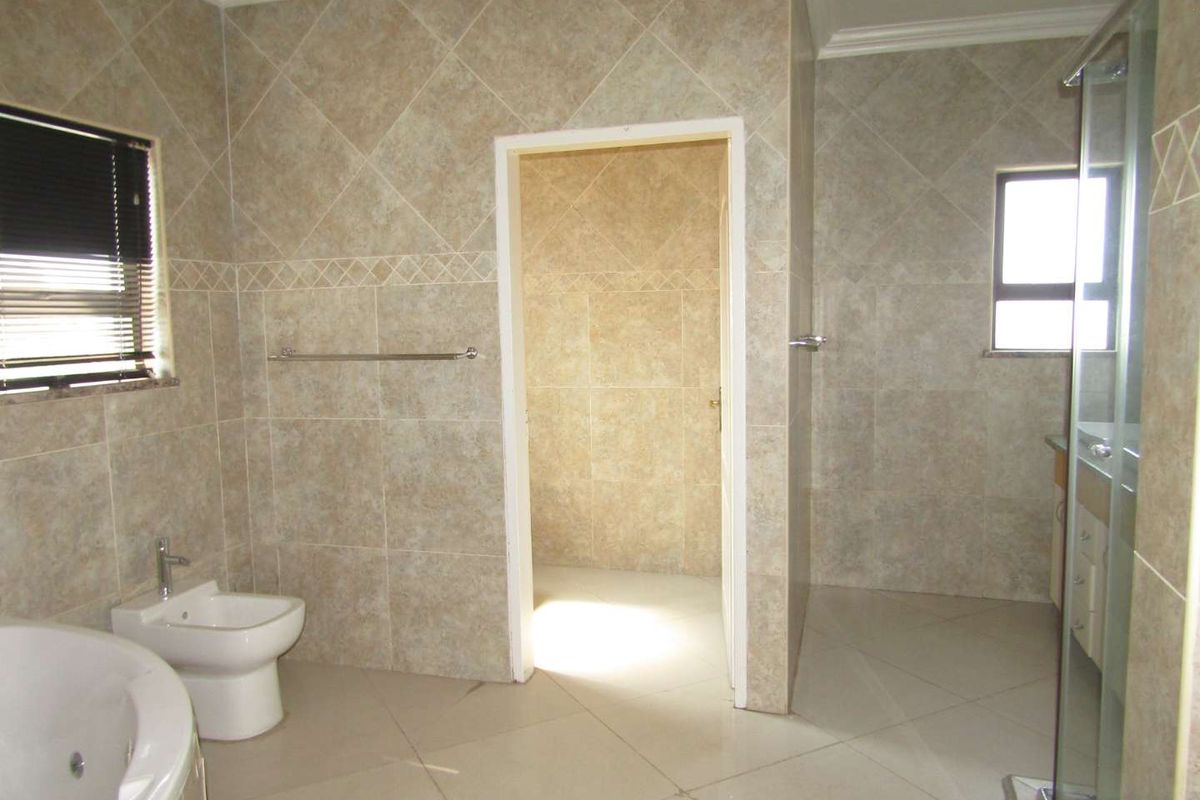 A spacious bathroom featuring neutral floor-to-ceiling wall tiles, a corner bathtub, a bidet, and a separate glass-enclosed shower area.