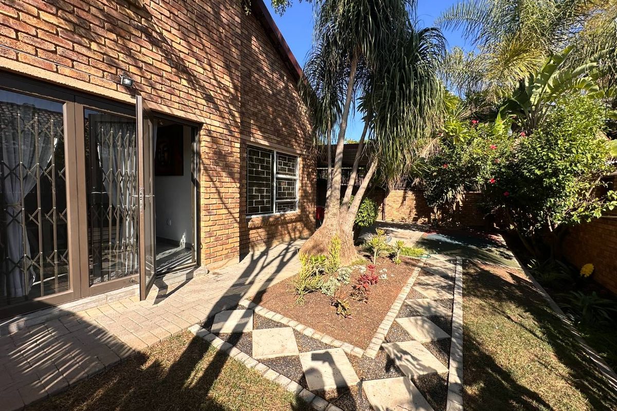 A private rear garden featuring a paved patio area, established landscaping, and a brick townhouse facade with secure access points.