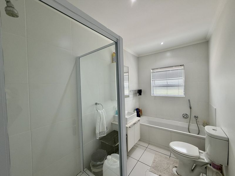 A clean, modern bathroom featuring a separate shower enclosure, a bathtub with handheld mixer, a vanity basin, and neutral tiled finishes.
