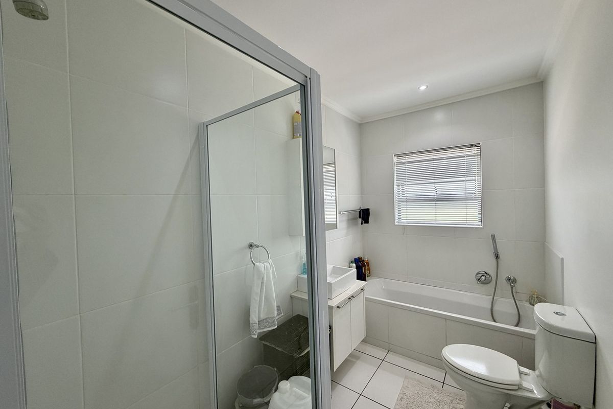 A clean, modern bathroom featuring a separate shower enclosure, a bathtub with handheld mixer, a vanity basin, and neutral tiled finishes.
