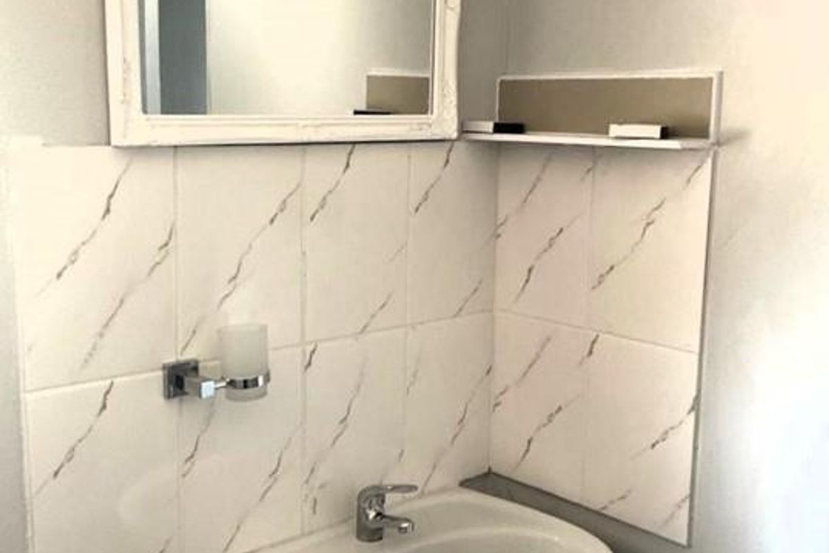 A compact bathroom vanity area featuring a wall-mounted ceramic basin, marble-effect tiled splashback, and a decorative framed mirror.
