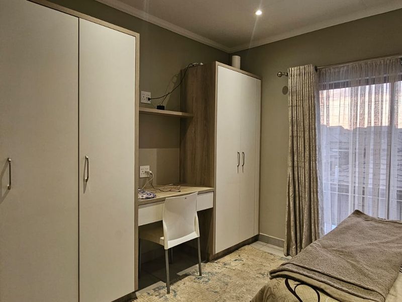 A well-maintained bedroom featuring built-in cupboards, an integrated desk workspace, and a sliding door providing access to the exterior.
