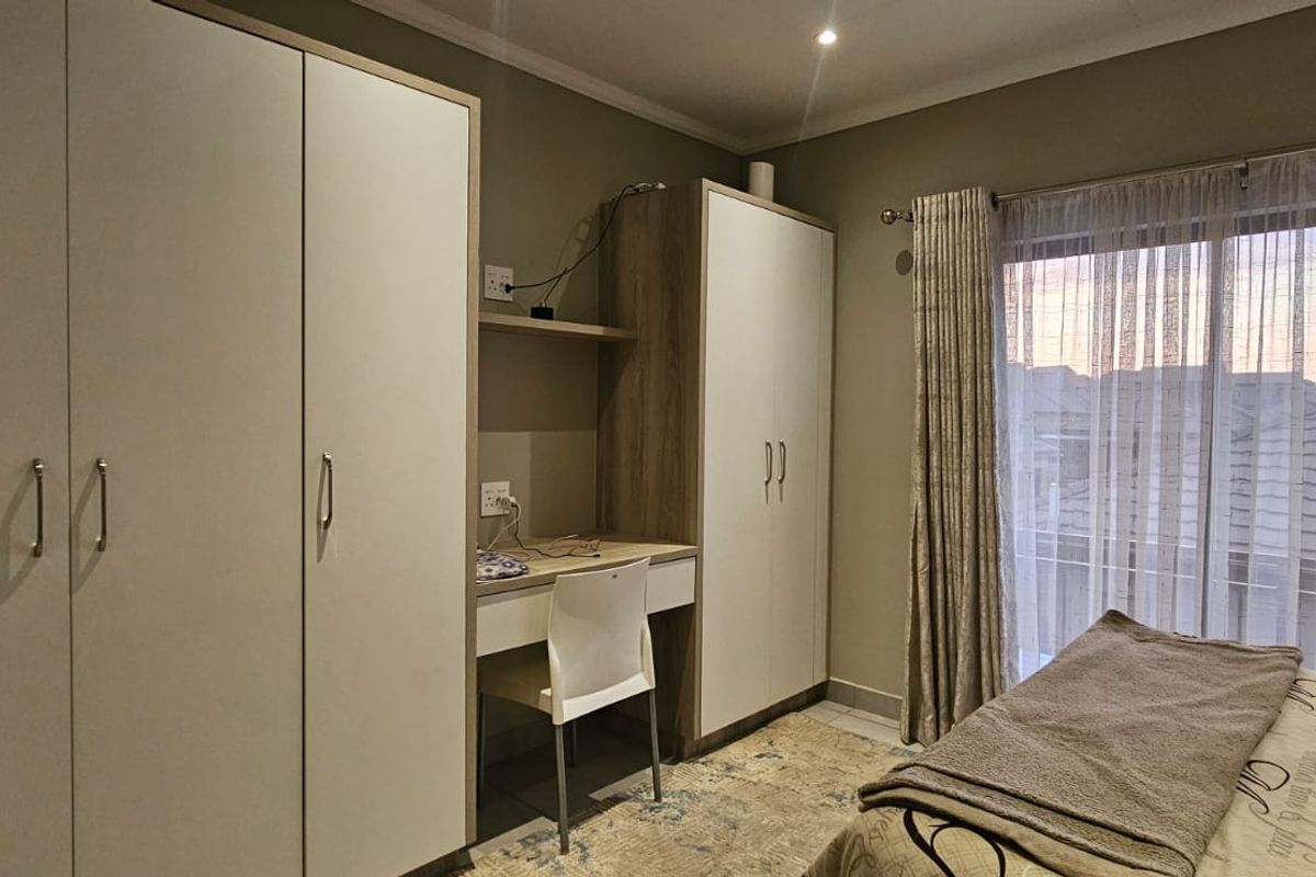 A well-maintained bedroom featuring built-in cupboards, an integrated desk workspace, and a sliding door providing access to the exterior.