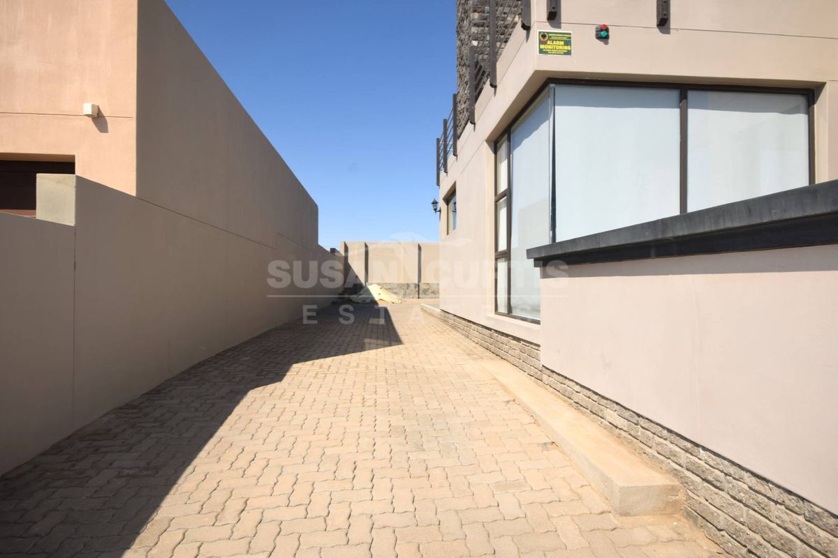 A paved side access path or driveway area featuring modern exterior wall finishes, large glass windows, and an integrated security alarm system.