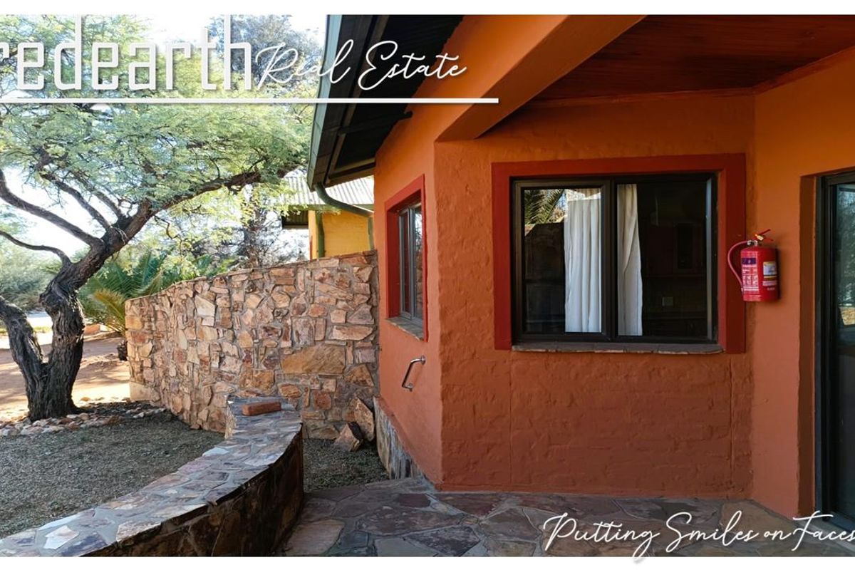 Rear exterior view featuring a stone paved patio, stone retaining wall, and a covered entrance area with a mounted fire extinguisher.