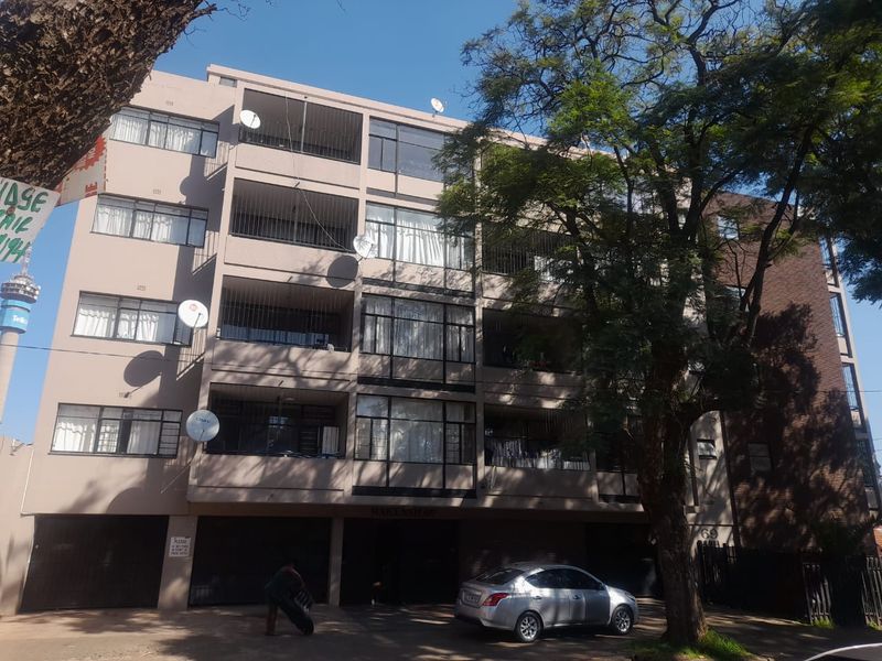 Front elevation of a multi-story apartment building featuring balconies, security bars, and ground-level parking facilities.