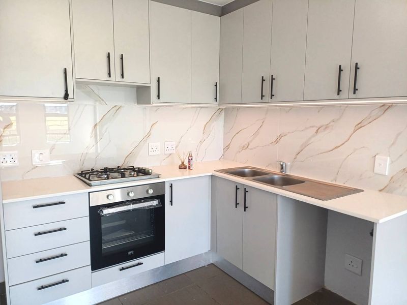 Modern kitchen featuring light grey cabinetry, quartz countertops, marble-look splashback, built-in gas hob, and oven with integrated under-cabinet lighting.