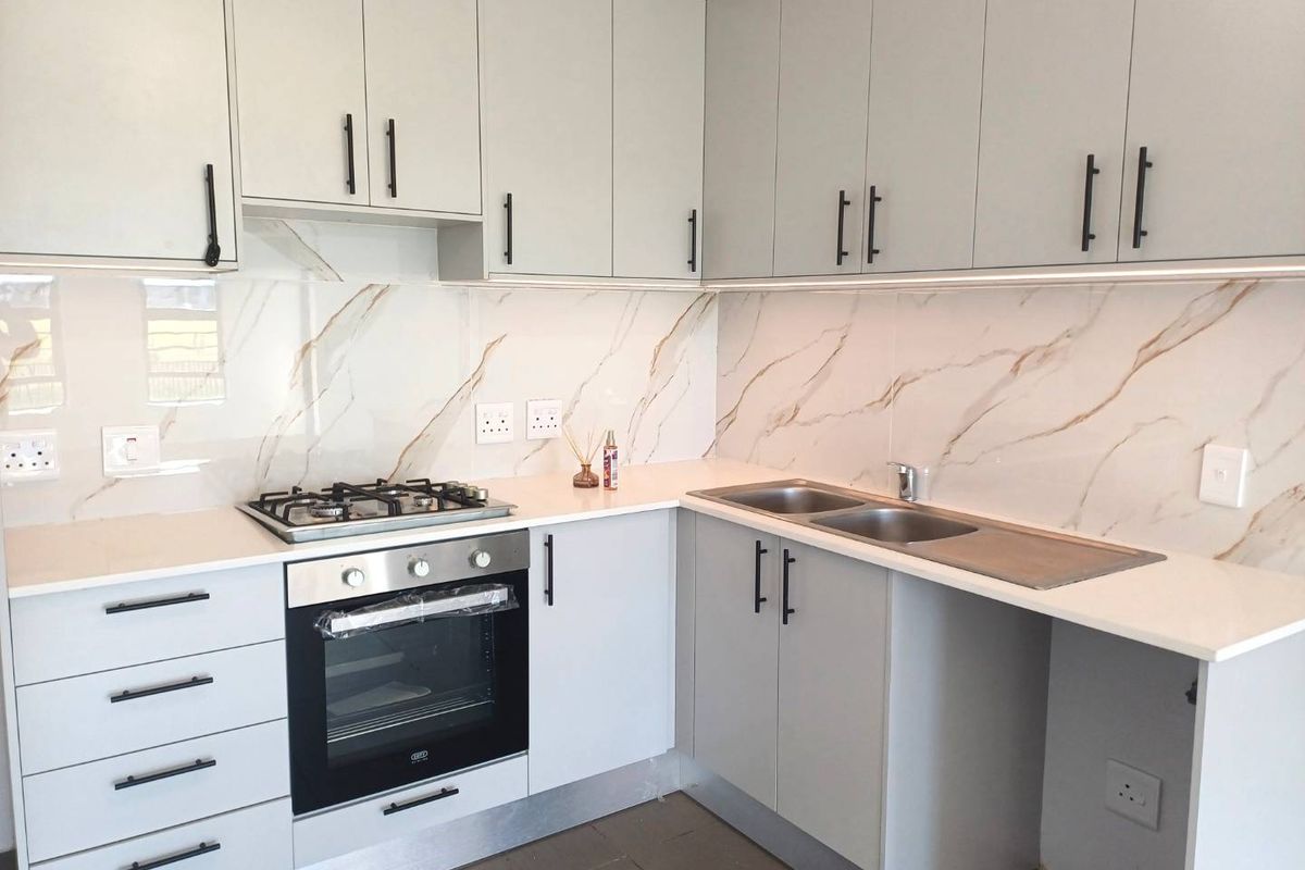 Modern kitchen featuring light grey cabinetry, quartz countertops, marble-look splashback, built-in gas hob, and oven with integrated under-cabinet lighting.