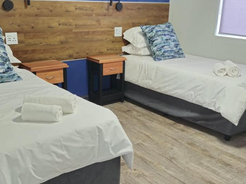 A well-maintained bedroom featuring wood-look laminate flooring, a decorative wood-panel headboard, and wall-mounted lighting fixtures.