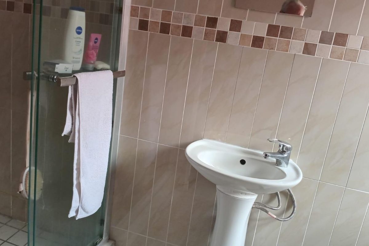 A functional bathroom featuring a pedestal basin with a chrome mixer tap and a glass-enclosed shower area with neutral ceramic wall tiling.