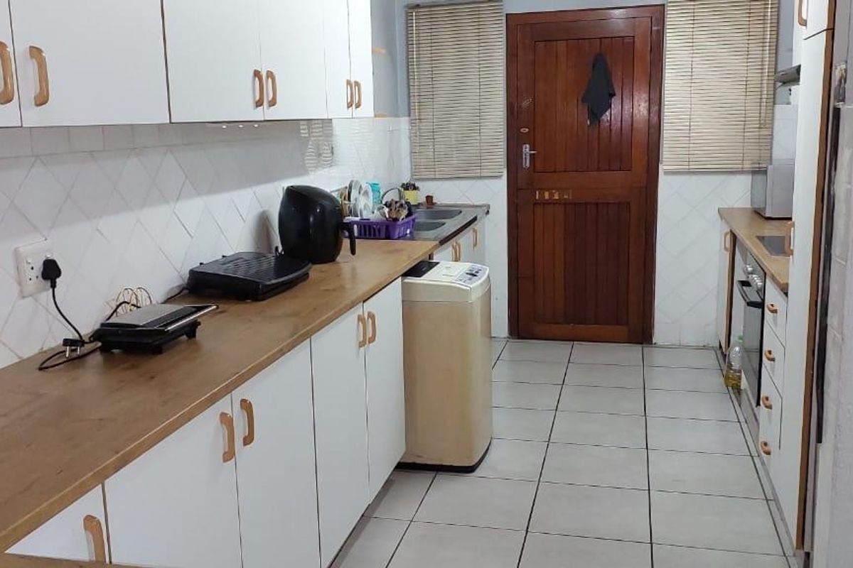Functional kitchen featuring white cabinetry, wood-look laminate countertops, tiled backsplash, and ceramic floor tiles with direct access to an exterior door.