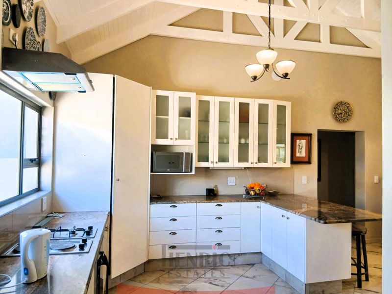 A well-appointed kitchen featuring white cabinetry, stone countertops, a gas hob with extractor, and a high vaulted ceiling with exposed trusses.