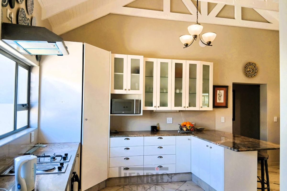 A well-appointed kitchen featuring white cabinetry, stone countertops, a gas hob with extractor, and a high vaulted ceiling with exposed trusses.