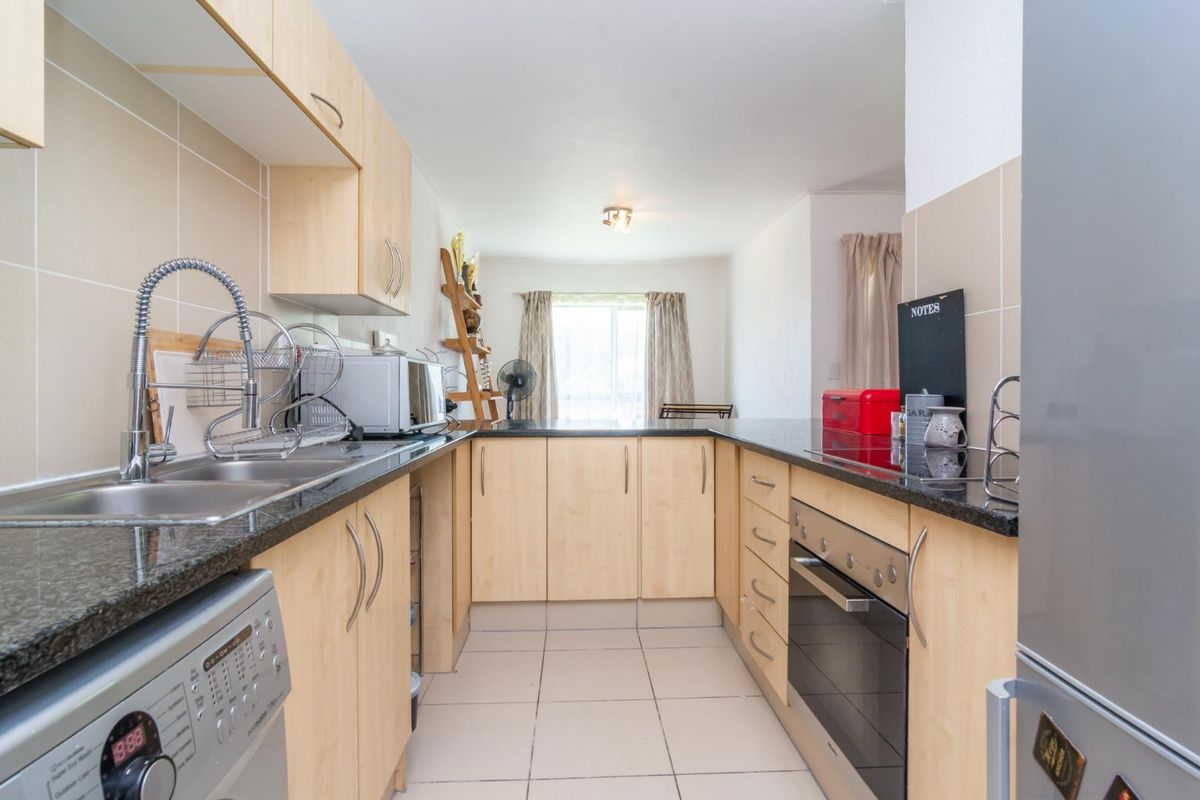 A functional galley-style kitchen featuring light wood cabinetry, dark granite countertops, tiled flooring, and integrated oven with hob.