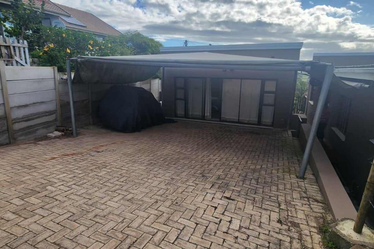 Rear exterior area featuring paved driveway, covered patio space with shade structure, and perimeter boundary walling.