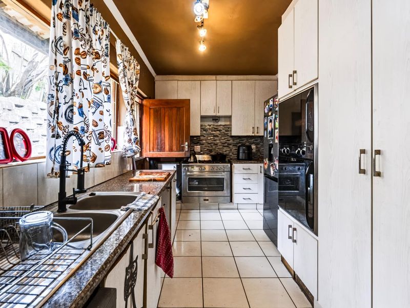 A functional kitchen featuring granite countertops, a double sink, built-in oven, hob, and ample cabinetry, with tiled flooring throughout.