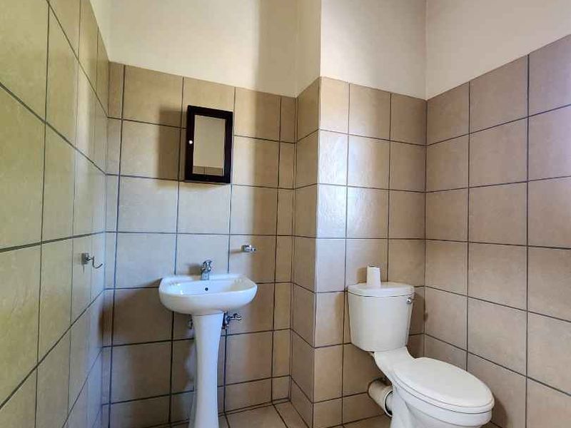 A functional bathroom featuring a pedestal basin, toilet, and neutral floor-to-ceiling tiling with exposed ceiling rafters.