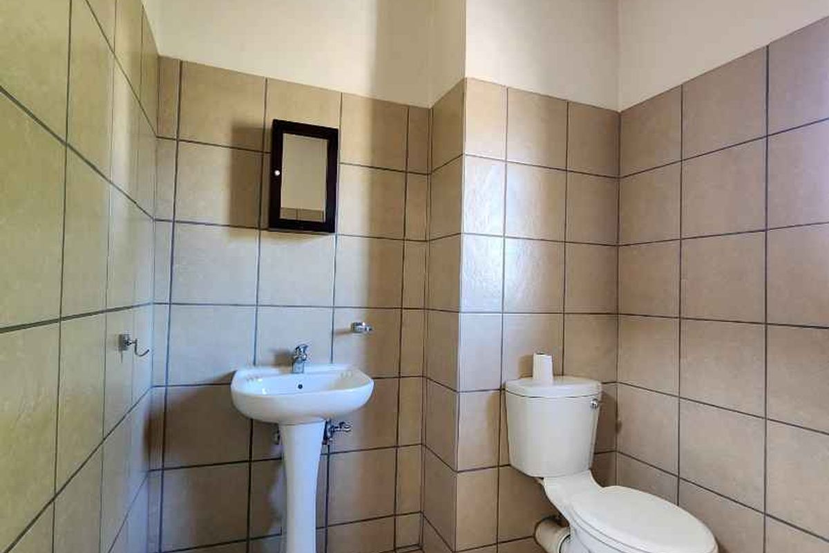 A functional bathroom featuring a pedestal basin, toilet, and neutral floor-to-ceiling tiling with exposed ceiling rafters.
