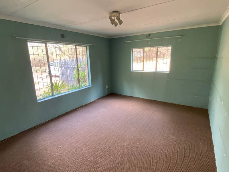 An empty bedroom featuring carpet flooring, security bars on the windows, and a neutral wall finish, offering a blank canvas for renovation.