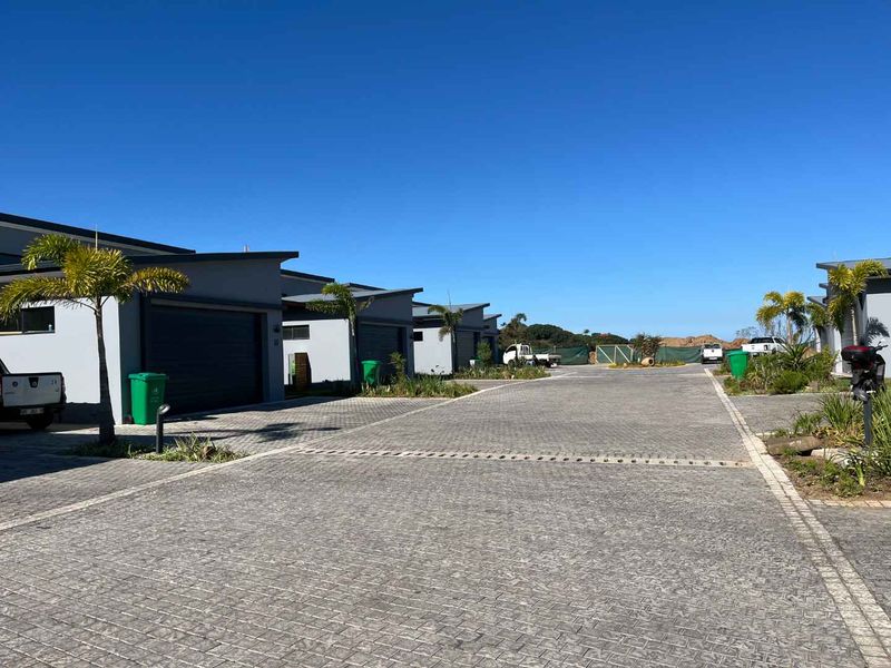 A view of the townhouse complex driveway featuring modern garage facades, paved surfaces, and landscaped areas under a clear blue sky.