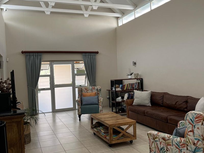 Spacious living room featuring high vaulted ceilings with exposed white trusses, clerestory windows for natural light, and neutral tiled flooring.