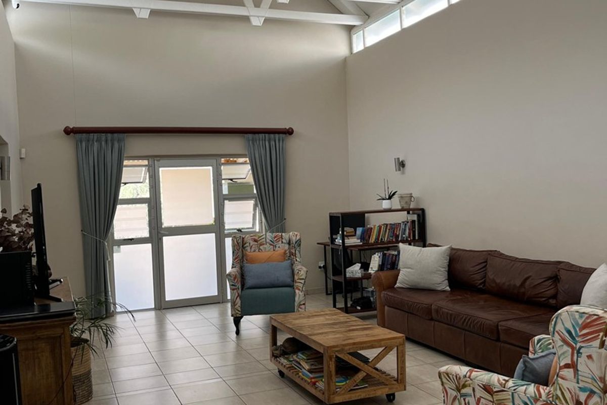 Spacious living room featuring high vaulted ceilings with exposed white trusses, clerestory windows for natural light, and neutral tiled flooring.