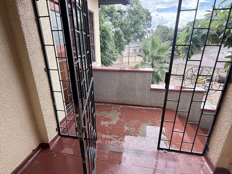 An outdoor balcony area featuring a security gate, low wall balustrade, and painted flooring showing signs of wear and peeling.