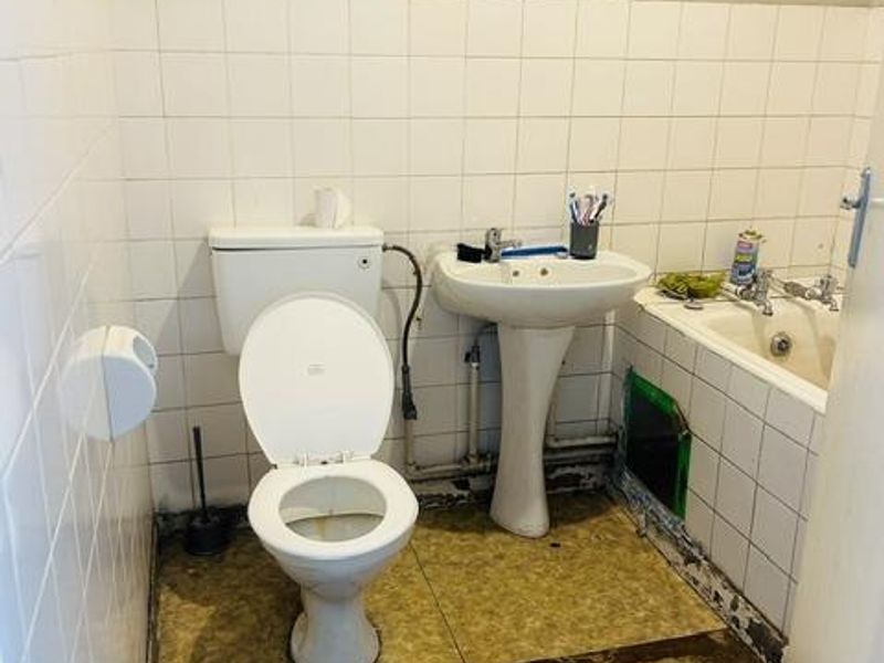 A dated bathroom requiring significant renovation, featuring a pedestal basin, toilet, and bathtub with visible wear to the flooring and wall finishes.