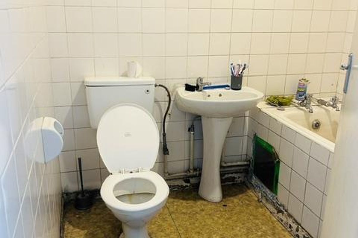 A dated bathroom requiring significant renovation, featuring a pedestal basin, toilet, and bathtub with visible wear to the flooring and wall finishes.