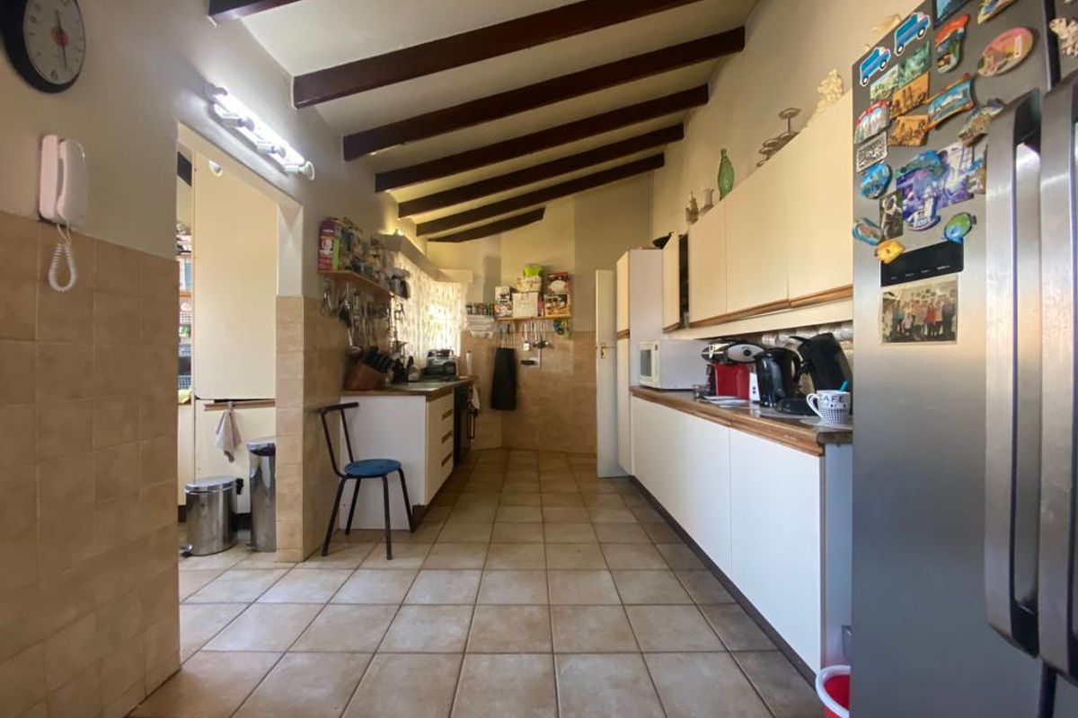 A functional galley-style kitchen featuring tiled flooring, exposed timber ceiling beams, and ample built-in cabinetry with tiled splashbacks.