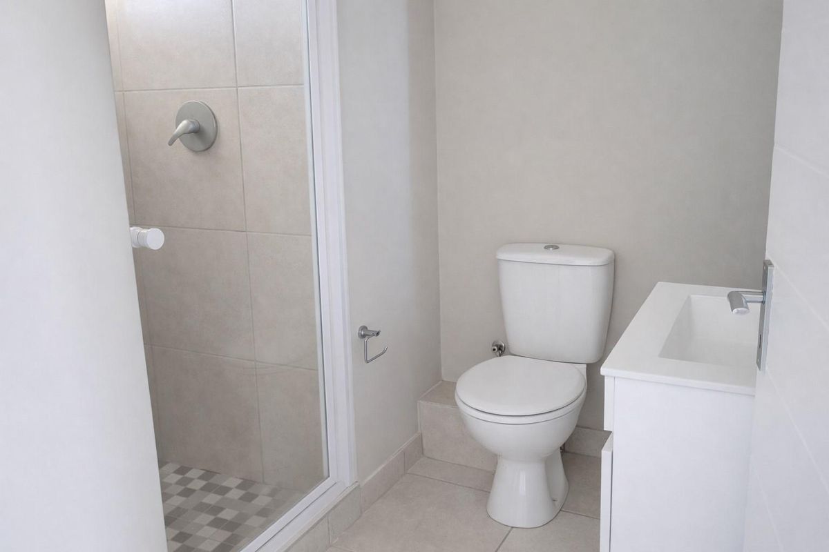 A clean, modern bathroom featuring a glass-enclosed shower with neutral tiling, a white vanity basin, and a standard toilet.