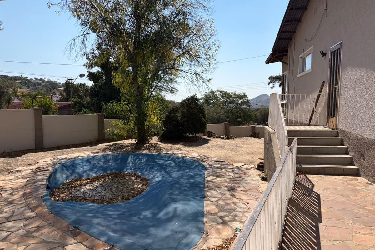 Outdoor pool area featuring stone paving, metal balustrades, and concrete stairs leading to the house, with a covered swimming pool and boundary wall.