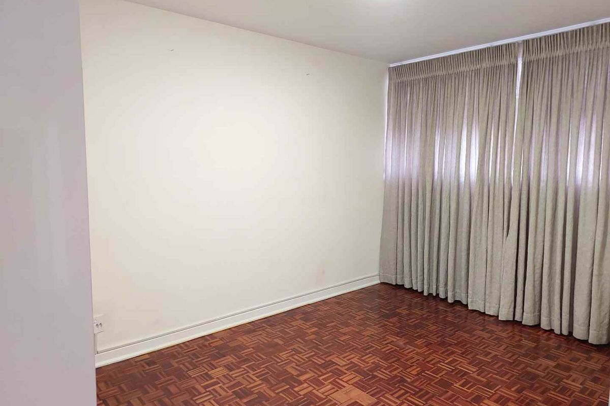 An empty bedroom featuring classic parquet flooring and full-length curtain tracks, offering a blank canvas for personalization.