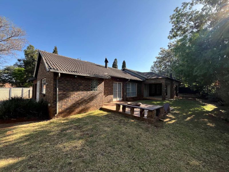 Rear view of a brick house featuring a tiled roof, a paved patio area with built-in brick seating, and a spacious garden.