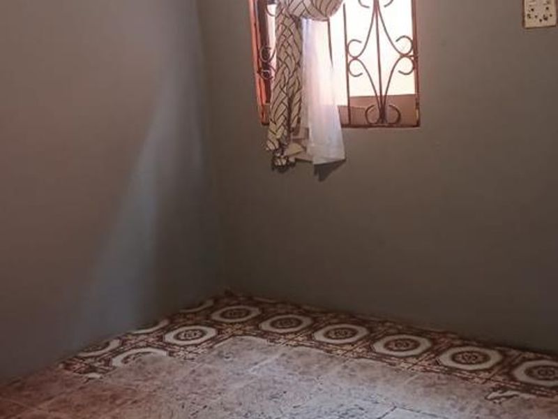An empty bedroom featuring tiled flooring, a window with security bars, and an exposed ceiling structure.