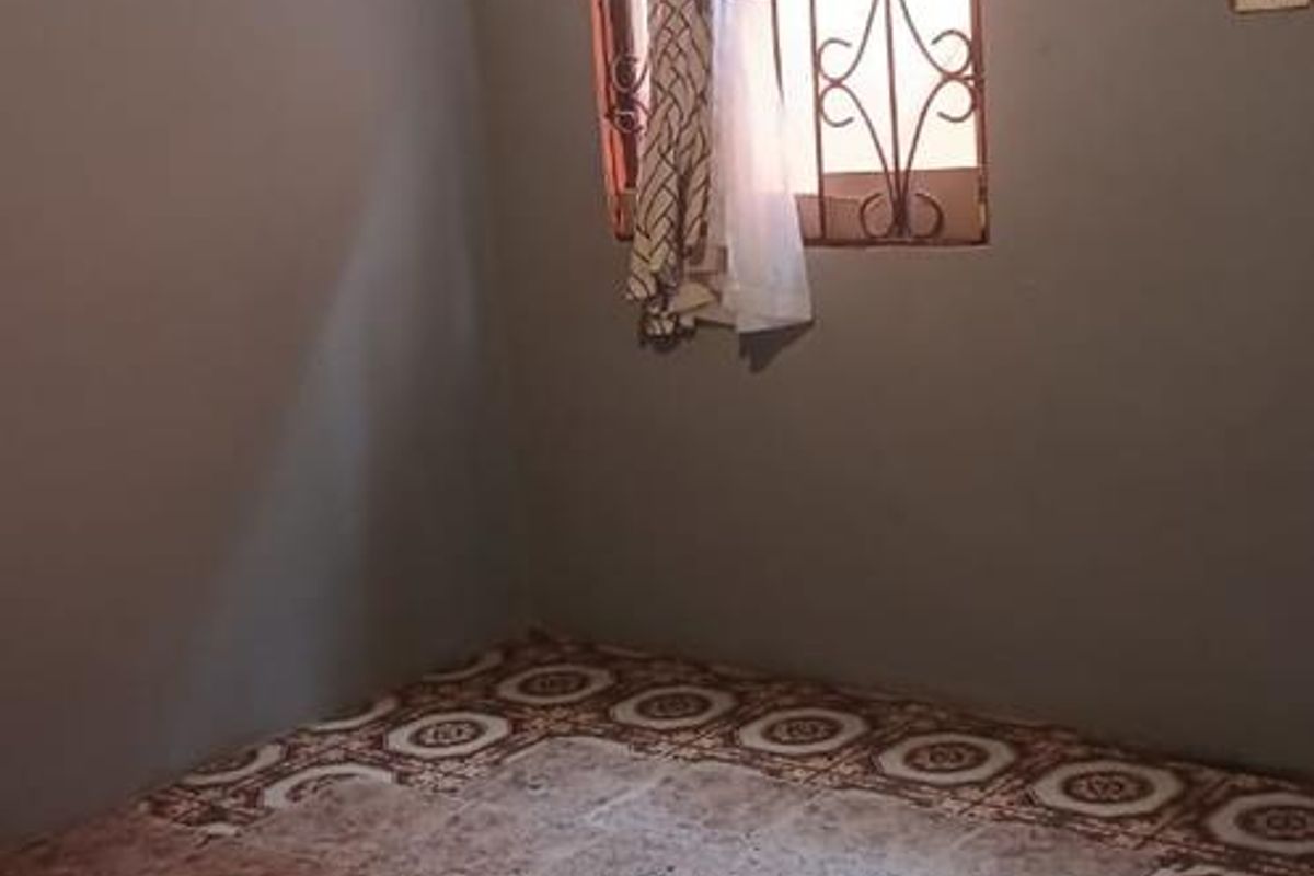 An empty bedroom featuring tiled flooring, a window with security bars, and an exposed ceiling structure.