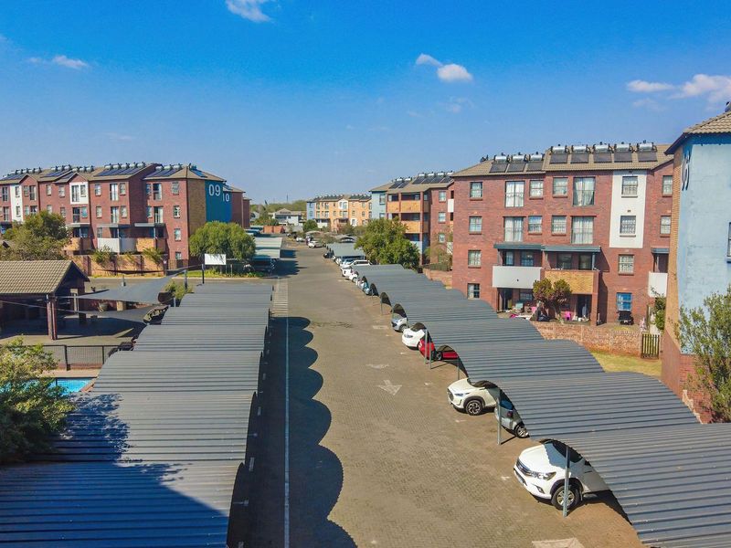 Aerial view of an apartment complex featuring multiple brick buildings, paved driveways, and rows of covered parking carports.