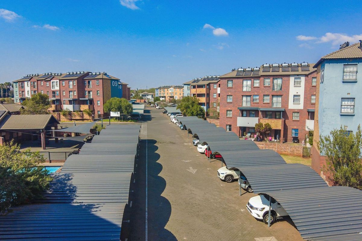 Aerial view of an apartment complex featuring multiple brick buildings, paved driveways, and rows of covered parking carports.