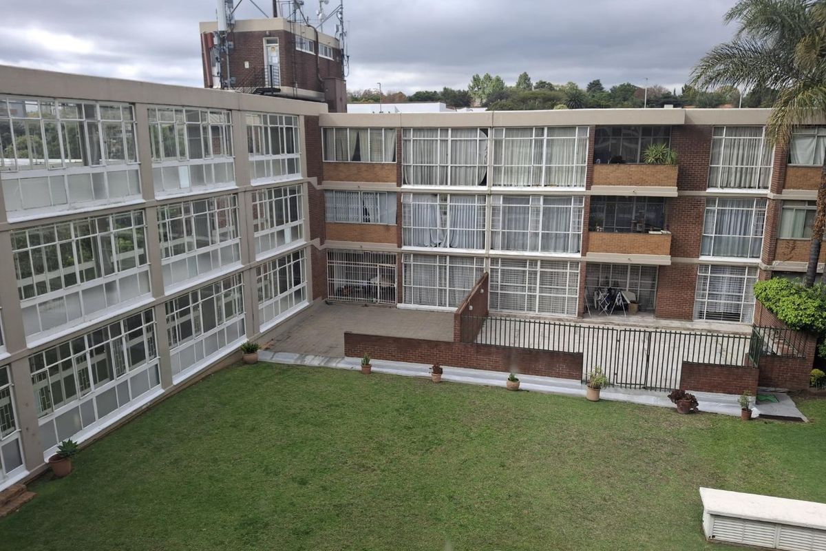 View of the apartment complex rear facade featuring brick construction, large windows, a paved courtyard area, and a shared communal garden space.