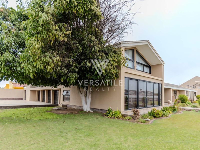 Rear view of the property featuring a large landscaped garden, paved driveway, and modern sliding glass doors leading into the home.