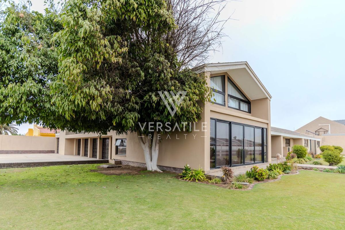 Rear view of the property featuring a large landscaped garden, paved driveway, and modern sliding glass doors leading into the home.