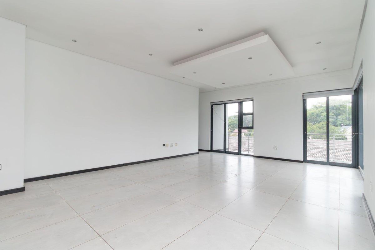 Spacious, light-filled living area featuring large format floor tiles, recessed ceiling detail with downlights, and sliding glass doors leading to an outdoor balcony.