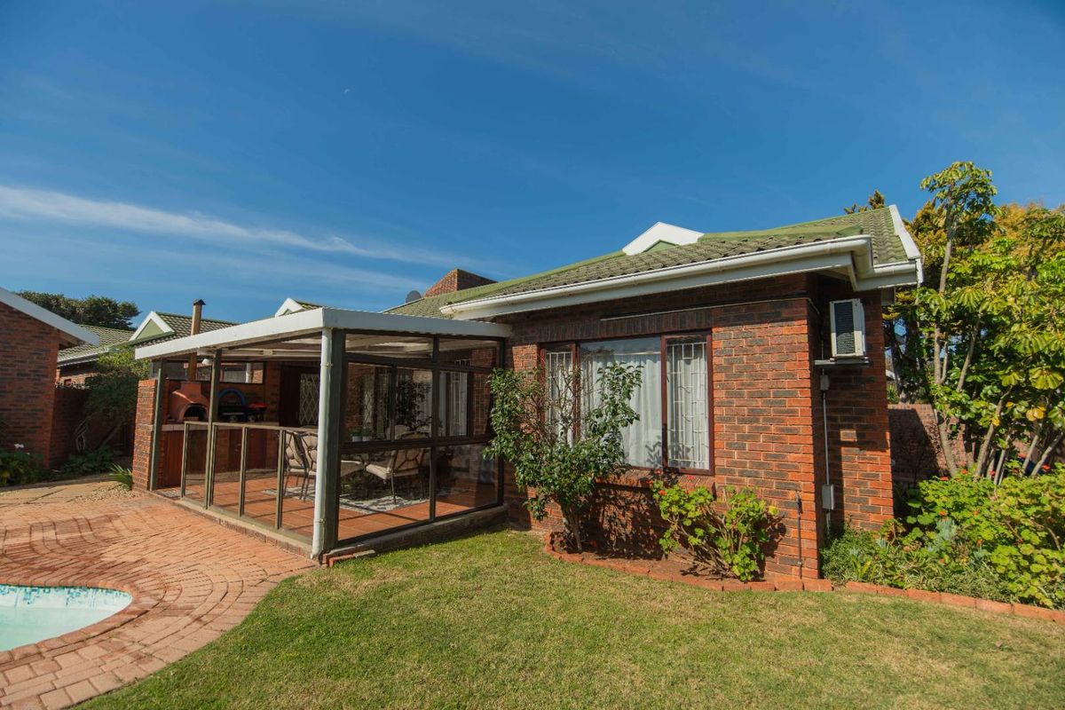 Rear view of a brick townhouse featuring an enclosed patio with a built-in braai, overlooking a paved pool area and garden.