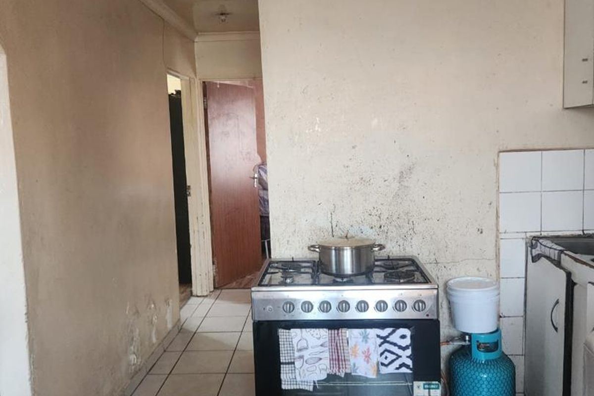 A dated kitchen area featuring a gas stove, tiled flooring, and splashback, currently requiring significant cosmetic updates and wall repairs.