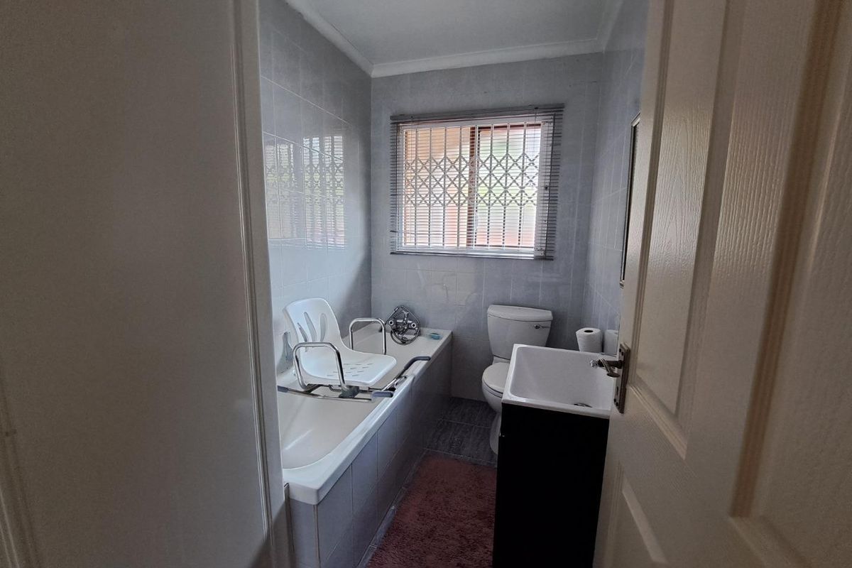 A functional bathroom featuring a bathtub, toilet, and vanity with tiled finishes and a window fitted with a security gate.