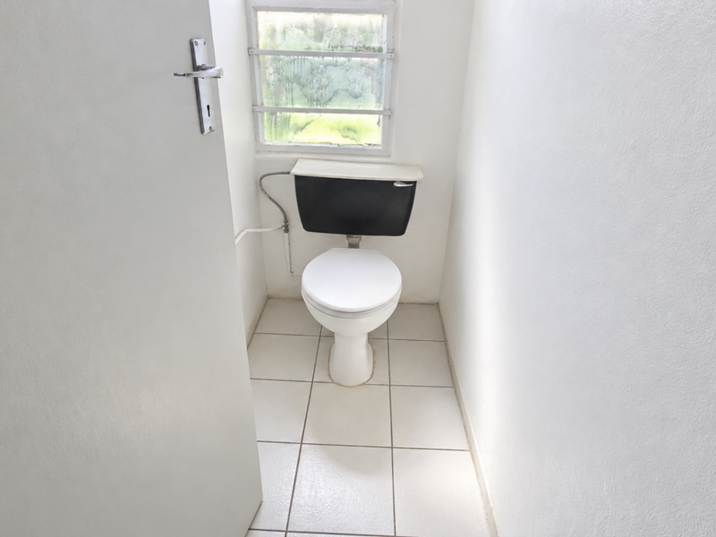 A small, functional restroom featuring a standard toilet, tiled flooring, and a louvered window providing natural light.