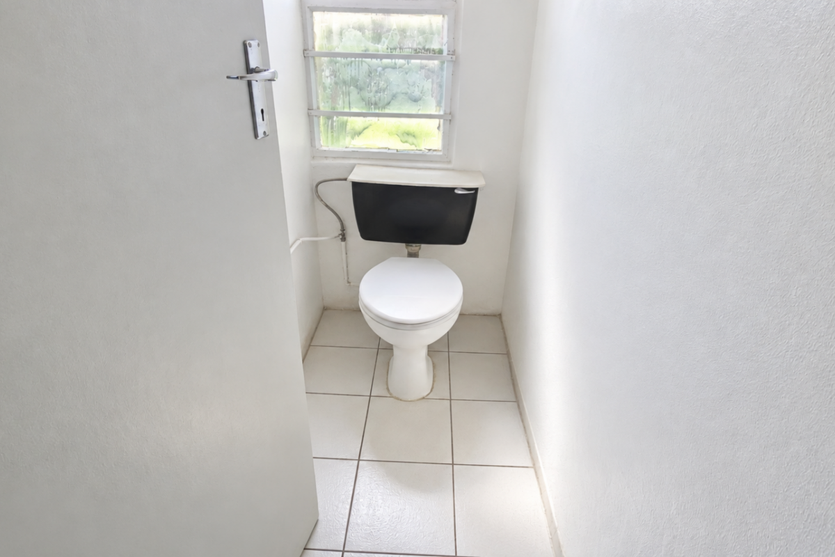 A small, functional restroom featuring a standard toilet, tiled flooring, and a louvered window providing natural light.